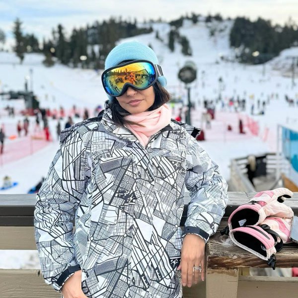 Adult in ski gear posing for the camera on the Snow Valley sundeck with mountain and riders in background